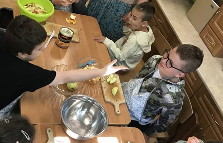 Uczniowie zgromadzeni wokól stołu wykonują sałatkę owocowa.