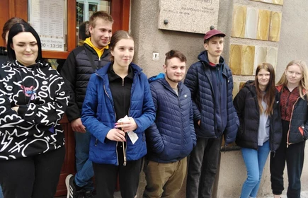 Grupa uczniów pozuje do zdjęcia przy wejściu do Powiatowej i Miejskiej Biblioteki Publicznej im. Jana Wiktora w Bochni.