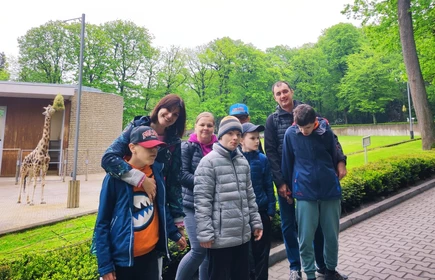 Grupa uczniów wraz z nauczycielami pozują do zdjęcia w ogrodzie zoologicznym w Krakowie.