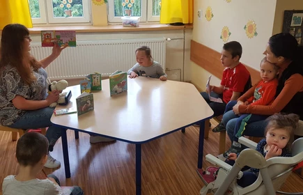 Nauczyciel siedzu przy stoliku z dziećmi, czyta książeczkę i pokazuje obrazki.