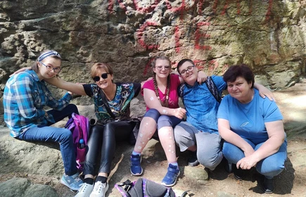 Grupa uczniów i opiekunów siedzi w otoczeniu skał - w rezerwacie przyrody &#34;Kamienie Brodzińskiego&#34;.