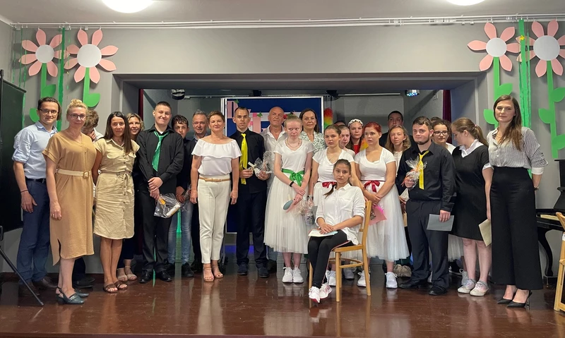 Młodzież kończąca szkołę, ubrana w eleganckie stroje pozuje do zdjęcia z nauczycielami w sali teatralnej SOSW w Bochni.