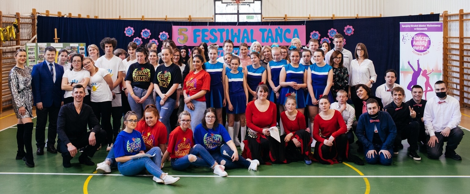 Dużą grupa , około 60 osób pozuje do zdjęcia w sali sportowej.