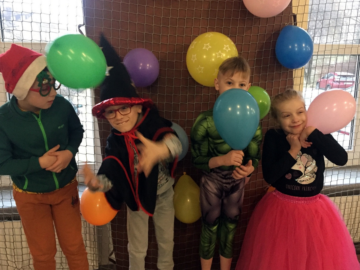 Czwórka dzieci przebrana w kolorowe stroje karnawałowe, trzyma w dłoniiach kolorowe balony.