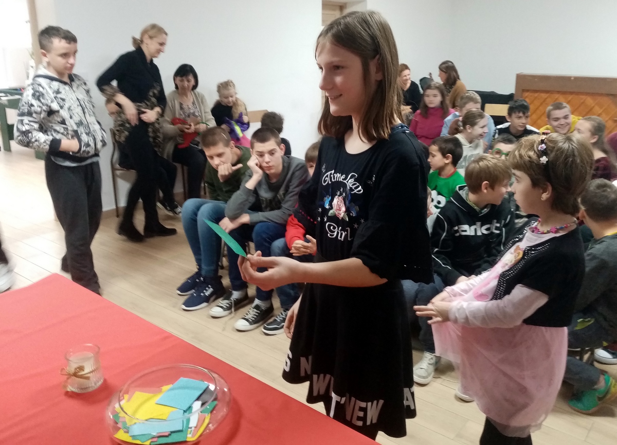 Dziewczynka stoi przed stołem, na którym rozłożone są wróżby andrzejkowe.