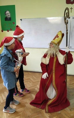 Święty Mikołaj i dwoje dziec w czapkach swiatecznych.