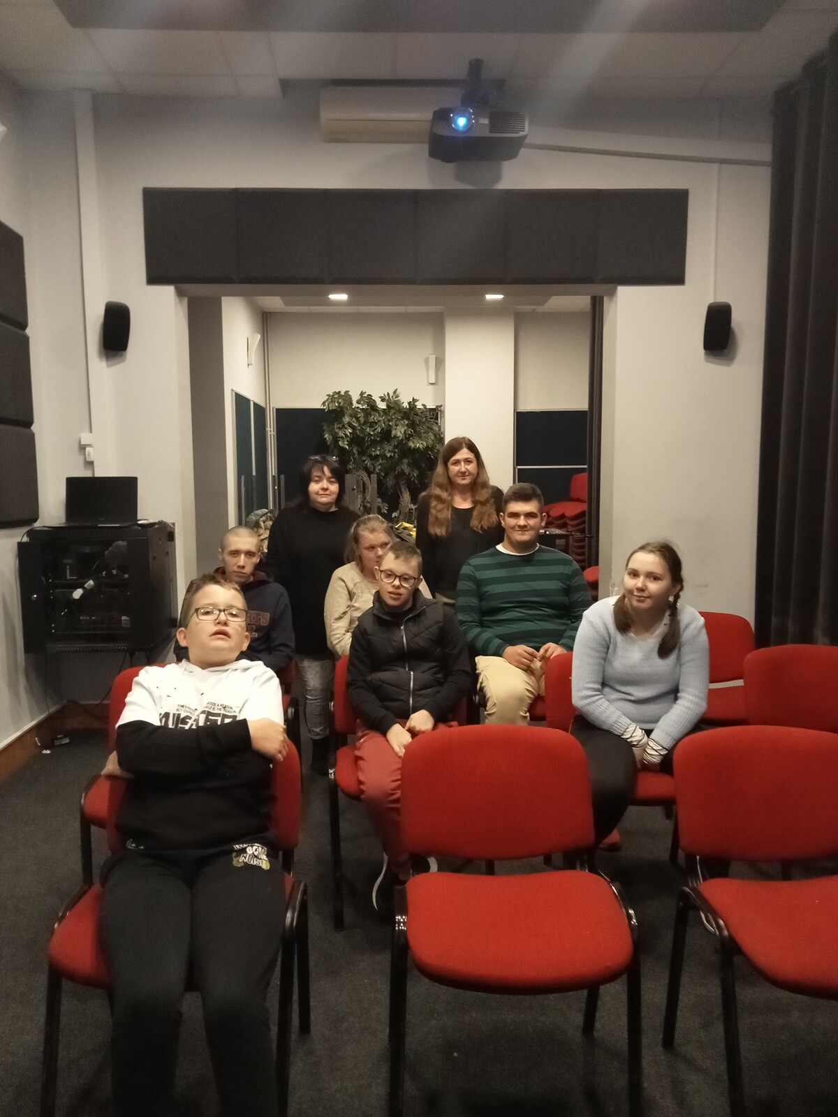 Uczniowie pozują do zdjęcia siedząc na krzesłach w sali kinowej.