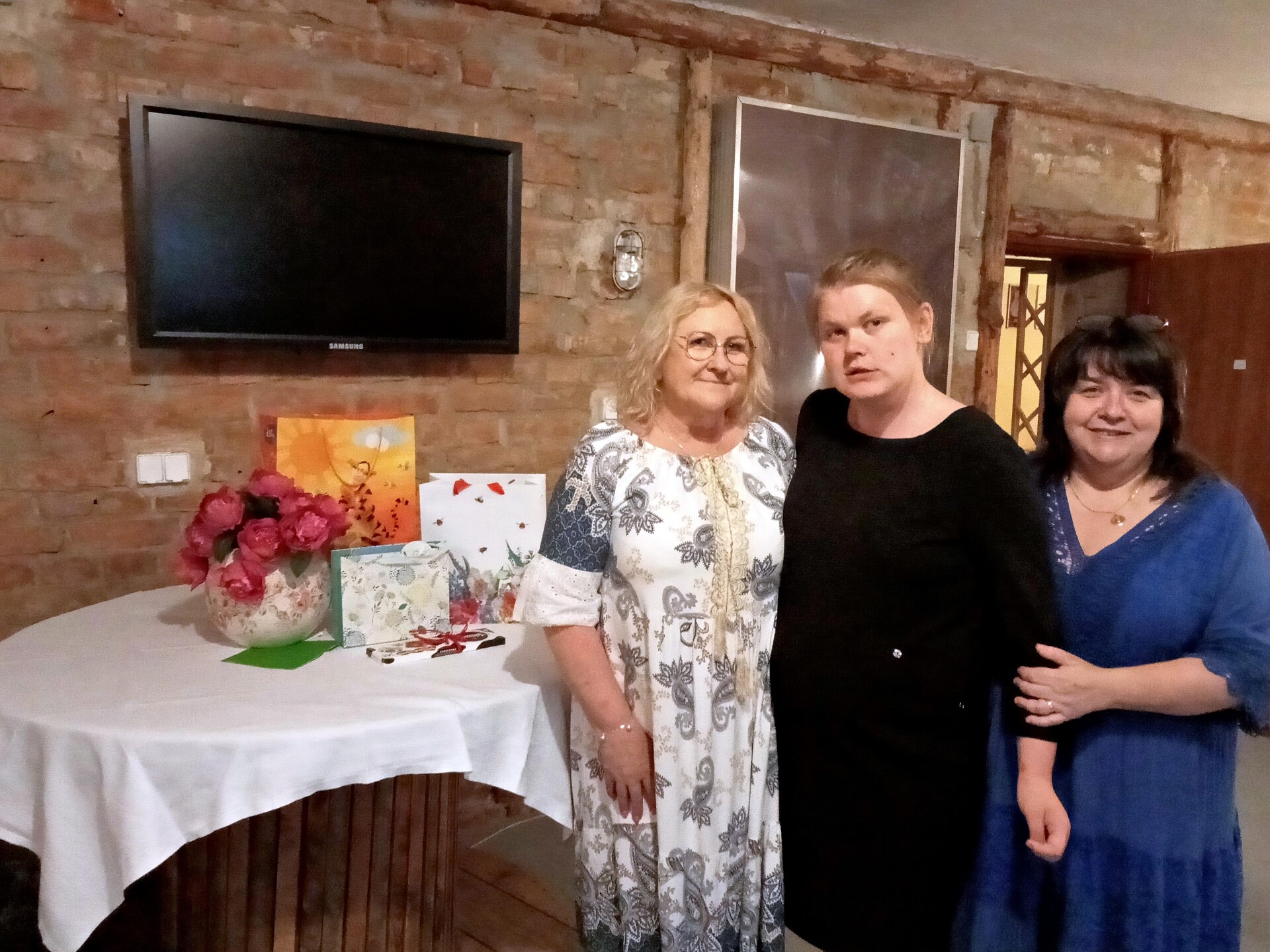 uczennica w czarnej sukience pozuje do zdjęcia z dwiema nauczycielkami w kawiarence szkolnej.