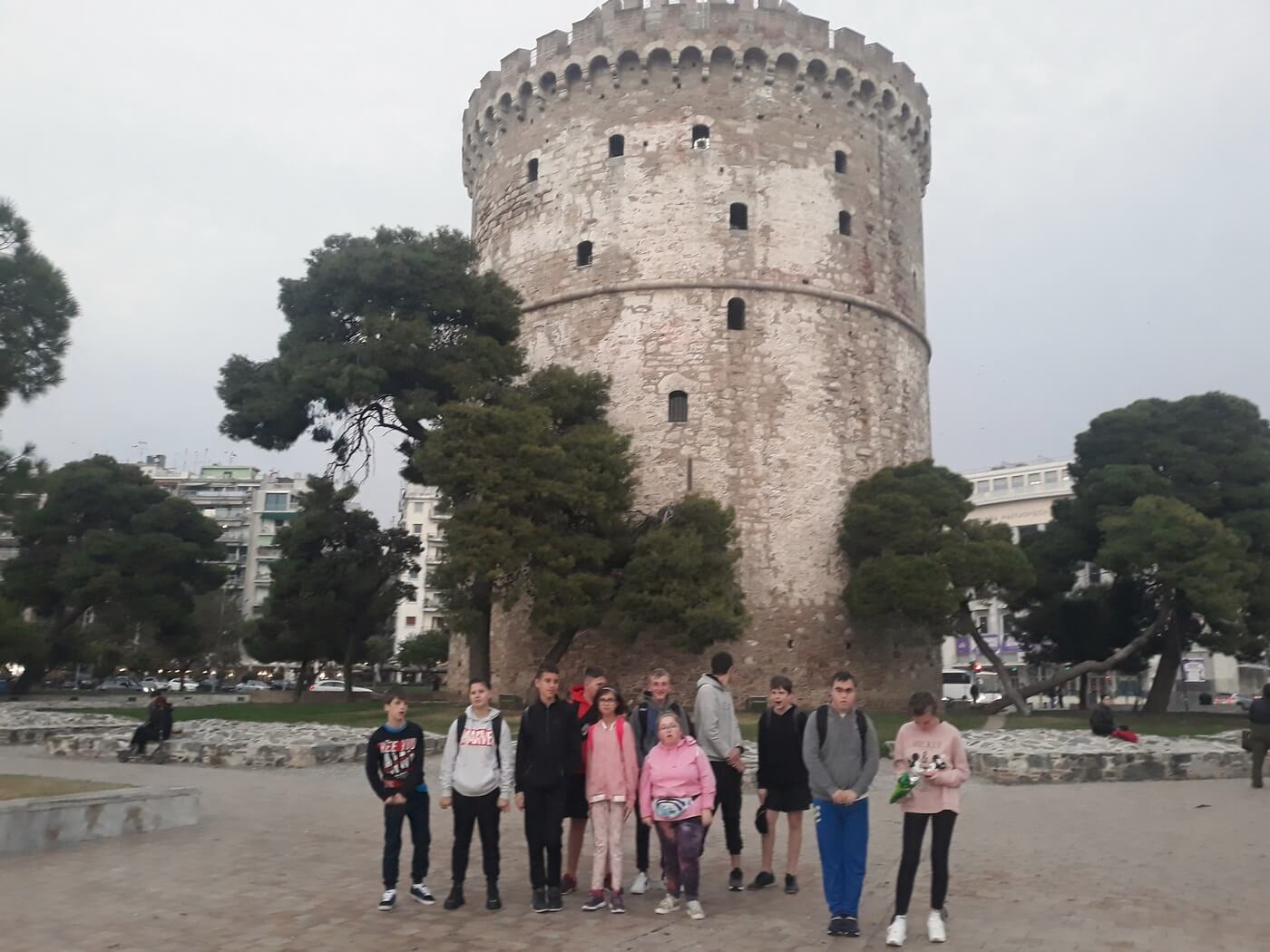 Grupa młodzieży stoi na tle Białej Wieży w Salonikach w Grecji.
