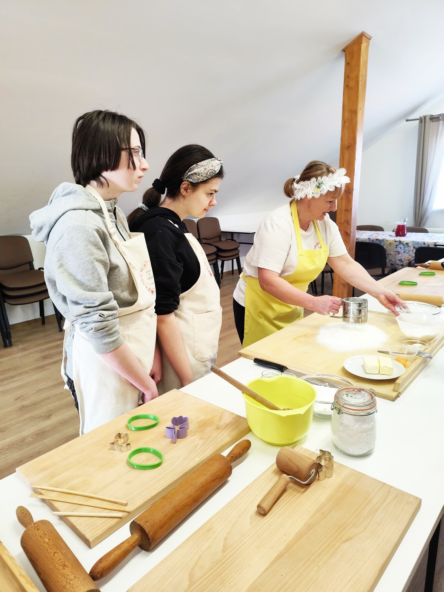 Dwie dziewczyny w fartuchach kuchennych i kucharka przygotowują ciastka przy stole kuchennym.