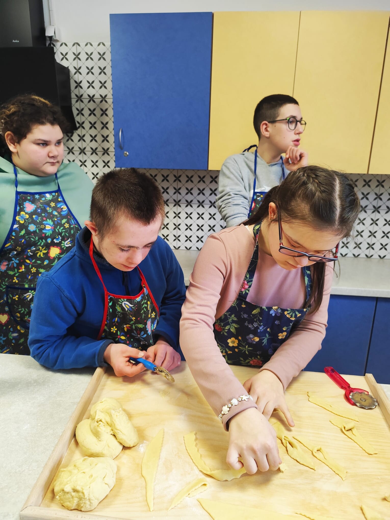 dziewzynka i chłopiec w kuchni wycinają faworki z ciasta.