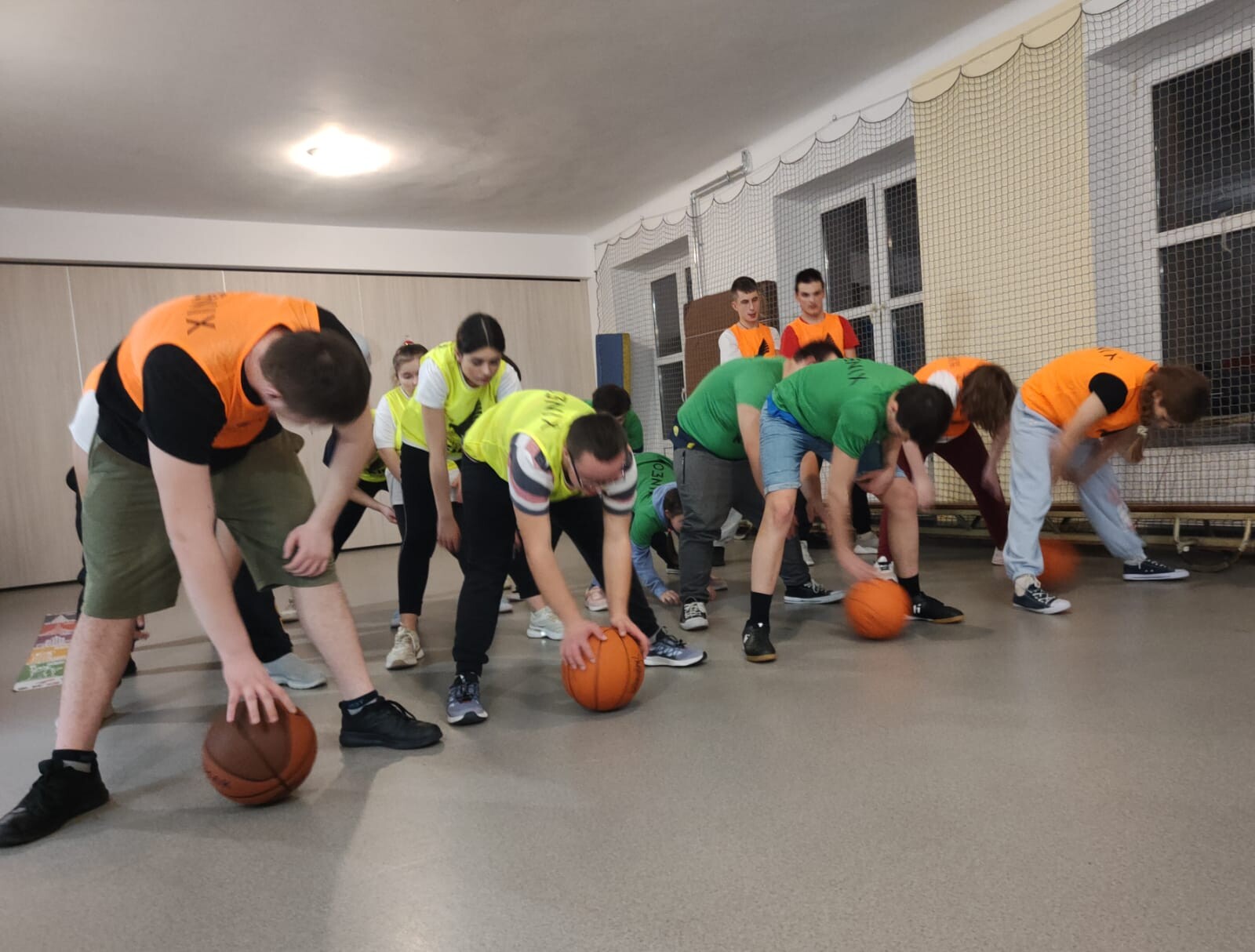 Grupa młodzieży w sportowych strojach wykonuje ćwiczenia z piłką do koszykówki.