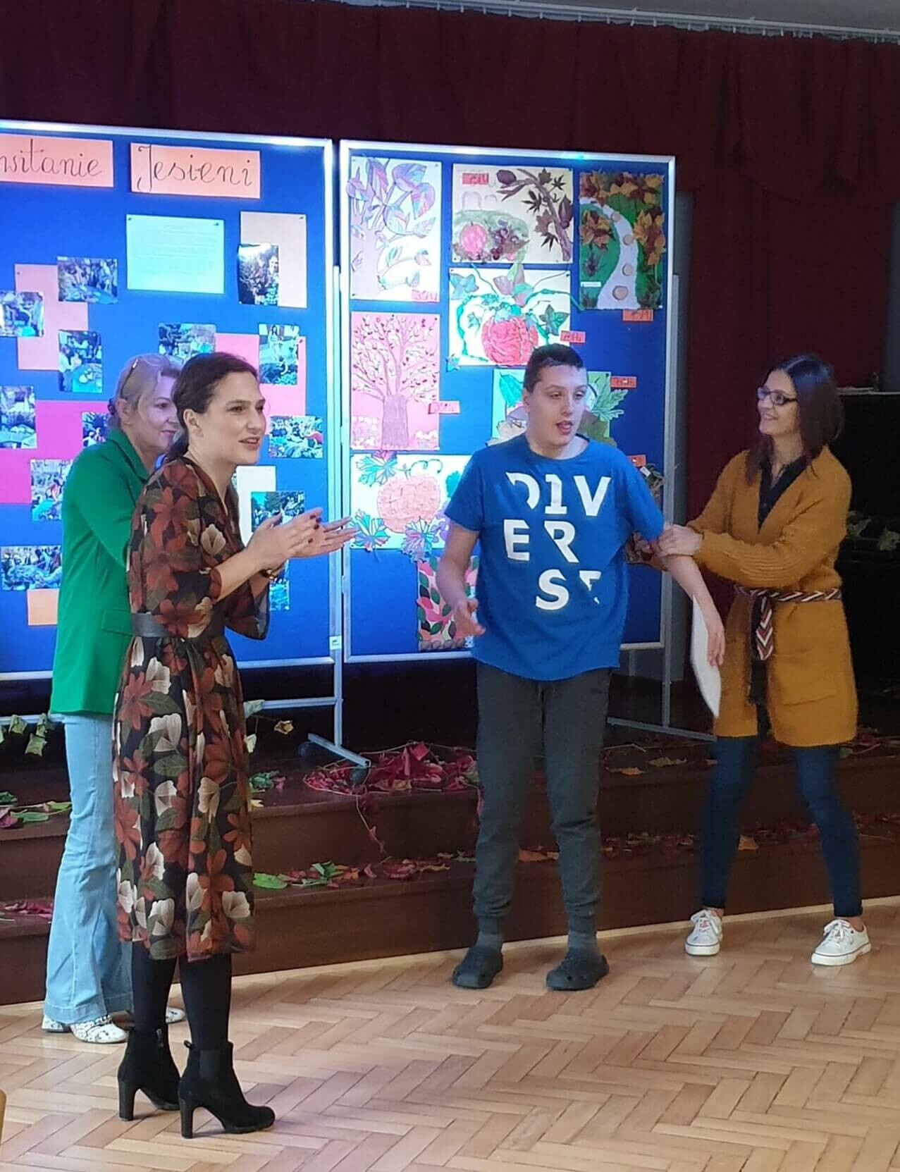 Chłopiec i trzy dorosłe kobiety stoją na scenie w sali teatralnej. W tle widać rozwieszone prace plastyczne.