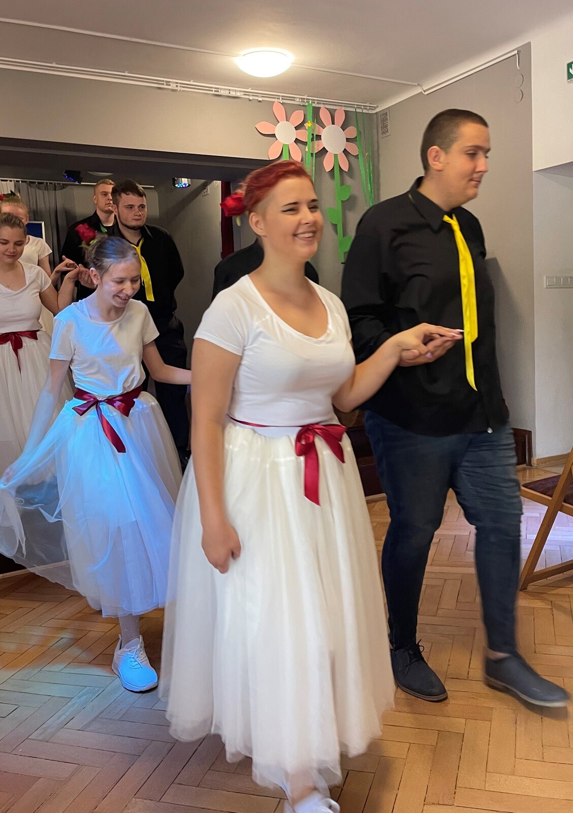 Dziewczyna ubrana na biało i chłopiec ubrany na czarno idą krokiem tanecznym.
