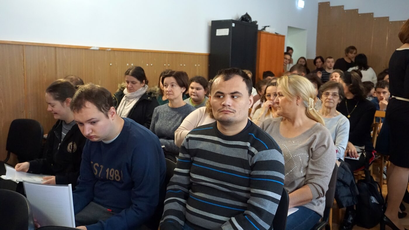 Grupa osób siedzi na krzesłach, oglądają spektakl.