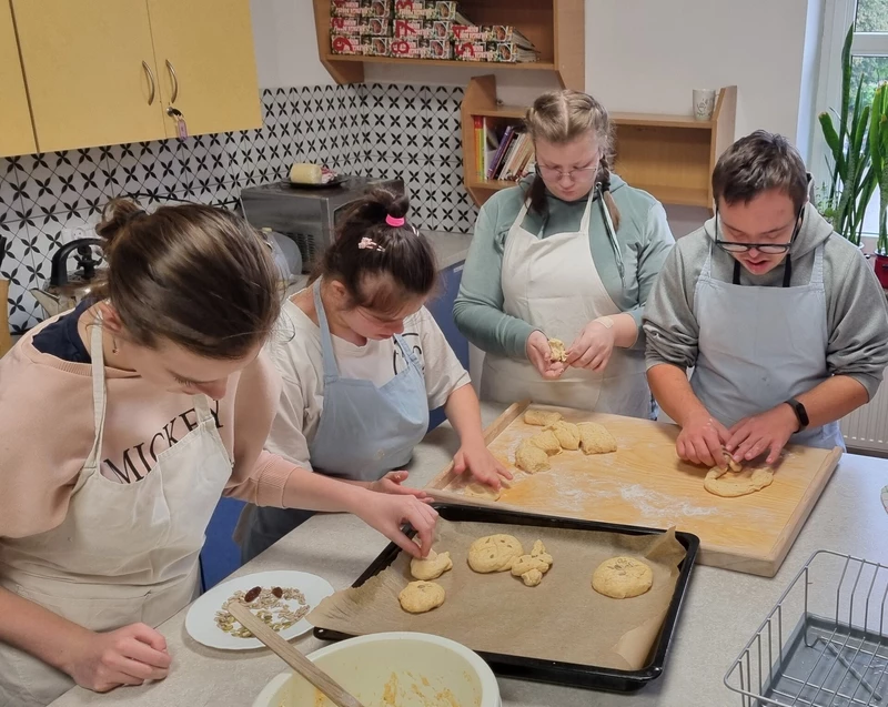 Czworo uczniów w fartuchach kucharskich wyplata z ciasta obwarzanki.