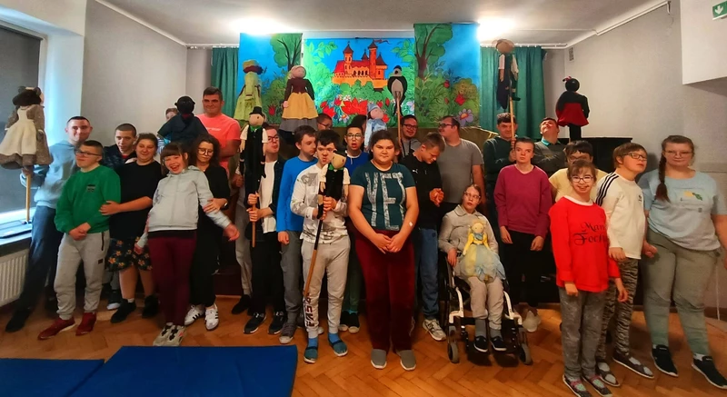 Grupa uczniów trzyma w rękach lalki teatralne, uśmiechają się.