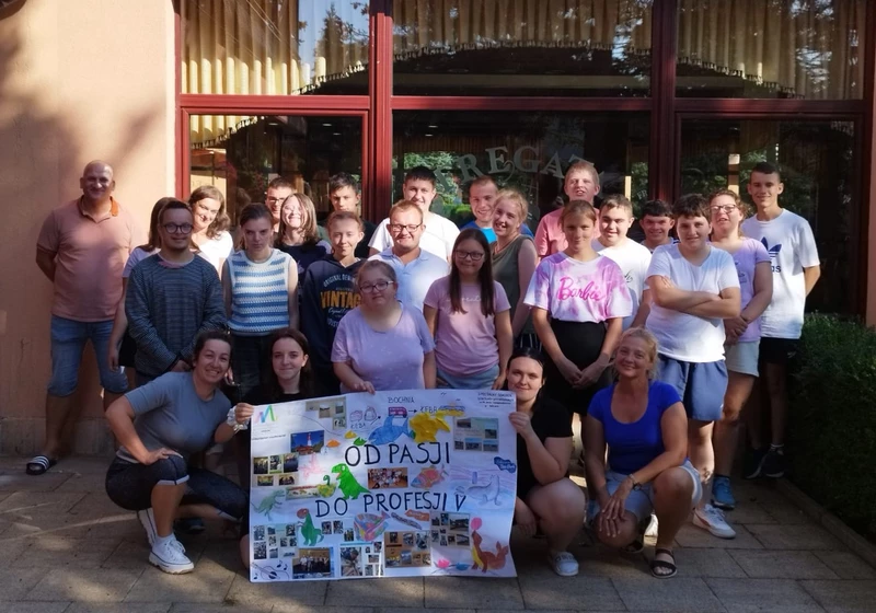 Grupa uczniów pozuje do zdjęcia. Młodzież stojąca na przodzie trzyma w dłoniach duży plakat, na którym jest napisane "Od pasji do profesji".