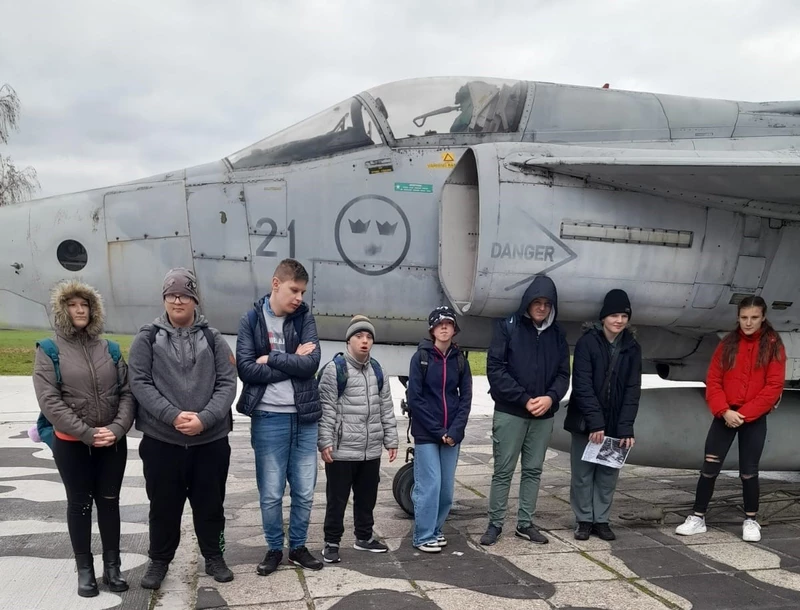 Grupa uczniów stoi na tle eksponatu samolotu w Muzeum Lotnictwa w Krakowie.