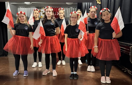 Uczennice ubrane w czerwone spódnice stoją na scenie w sali teatralnej SOSW w Bochni.