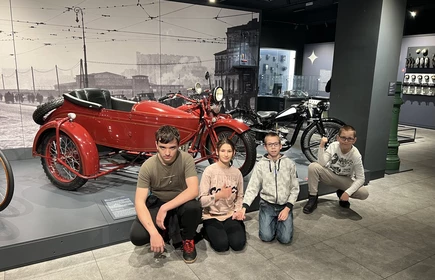 Czworo uczniów pozuje do zdjęcia w Muzeum Techniki i Inżynierii w Krakowie. W tle widać stare motocykle.