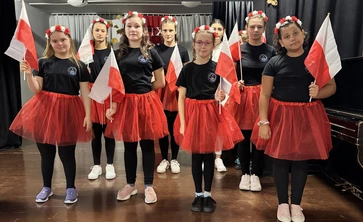 Uczennice ubrane w czerwone spódnice stoją na scenie w sali teatralnej SOSW w Bochni.