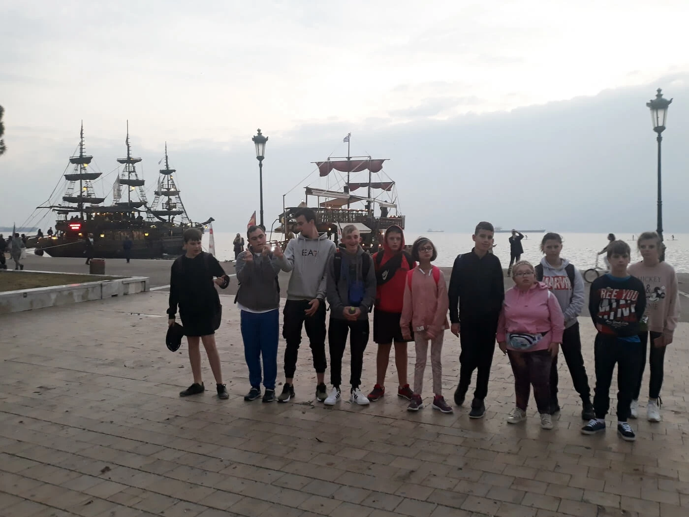 Grupa mlodziezy stoi na wybrzezu Morza Egejskiego. W tle widać statek.