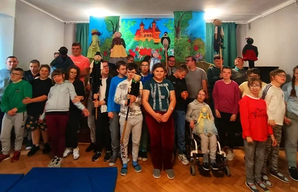 Grupa uczniów trzyma w rękach lalki teatralne, uśmiechają się.