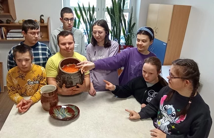 Uczniowie stoją wokół nlatu kuchennego, wskazują rekami na wypełniony  kapustą garnek kamionkowy.