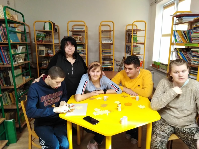 Uczniowie siedzą przy żółtym stoliku w bibliotece szkolnej, w tle widać regały z książkami.