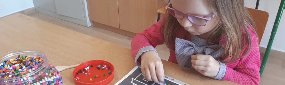 Dziewczynka w okularach siedzi przy stole i układa koraliki