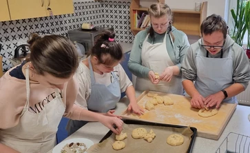 Czworo uczniów w fartuchach kucharskich wyplata z ciasta obwarzanki.