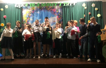 Uczniowie stoja na scenie w sali teatralnej.