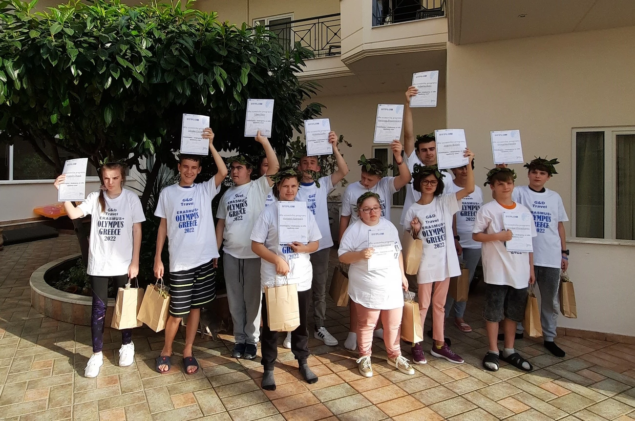 Grupa młodzieży pozuje do zdjęcia trzymając dyplomy w uniesionych nad głowy rękach