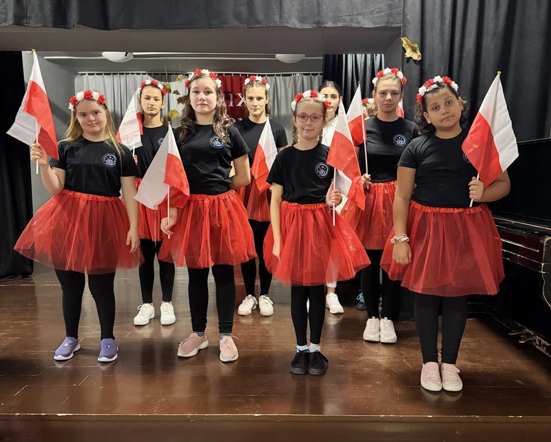 Uczennice ubrane w czerwone spódnice stoją na scenie w sali teatralnej SOSW w Bochni.