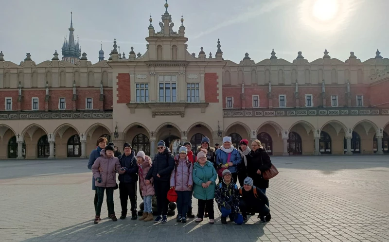 Grupa młodzieży pozuje do zdjęcia na tle Krakowskich Sukiennic.