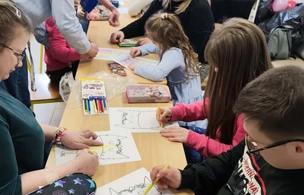 Uczniowie siedza przy jednym stoliku, malują taka sama ilustrację stworka.