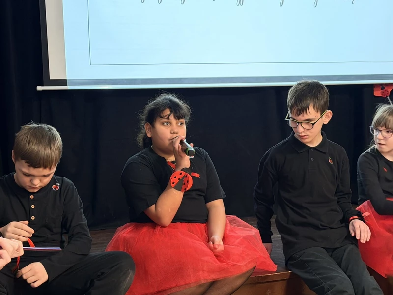 Dziewczynka siedzi na schodach,  mówi do mikrofonu, obok siedzi dwóch chłopców.