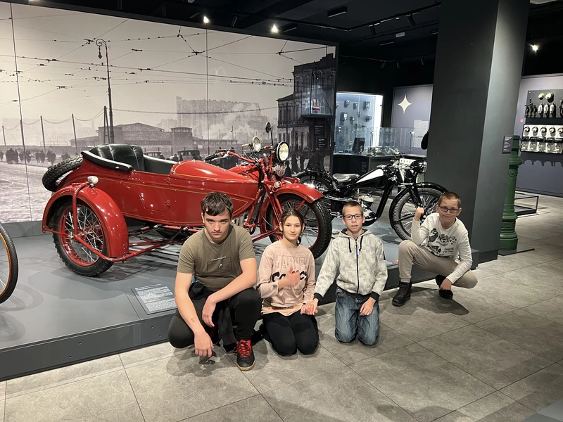 Czworo uczniów pozuje do zdjęcia w Muzeum Techniki i Inżynierii w Krakowie. W tle widać stare motocykle.