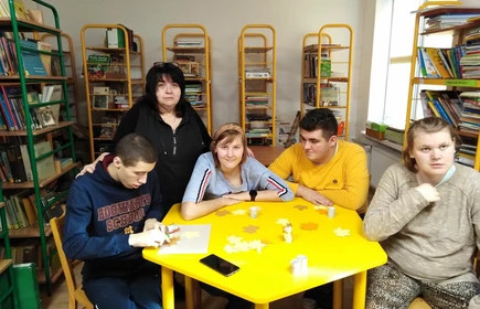 Uczniowie siedzą przy żółtym stoliku w bibliotece szkolnej, w tle widać regały z książkami.