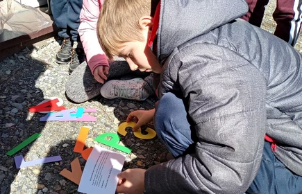 Chłopiec w kurtce kuca i układa napis z liter na ziemi.