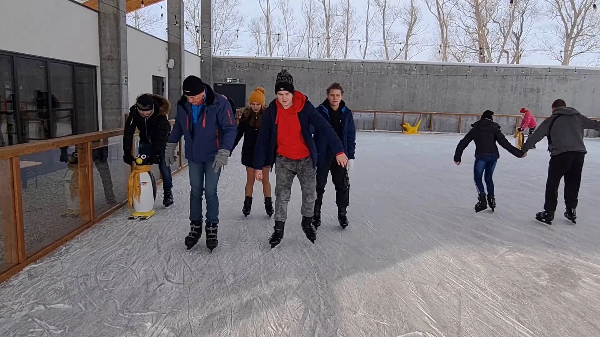 Grupa młodzieży jeżdzi na łyżwach na lodowisku w  komplewksie Kuter Port NIeznanowice.