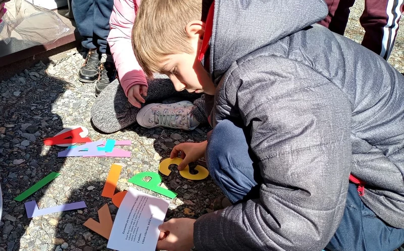 Chłopiec w kurtce kuca i układa napis z liter na ziemi.