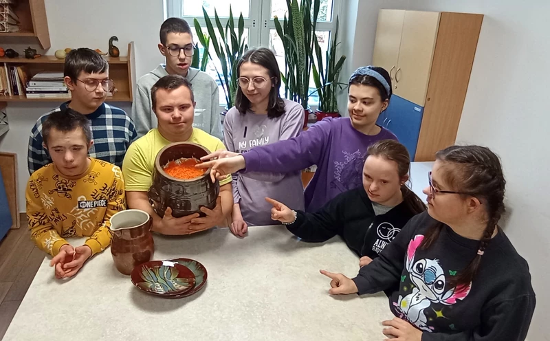 Uczniowie stoją wokół nlatu kuchennego, wskazują rekami na wypełniony  kapustą garnek kamionkowy.
