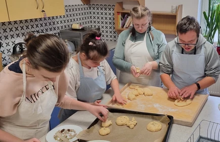 Czworo uczniów w fartuchach kucharskich wyplata z ciasta obwarzanki.