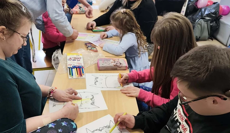 Uczniowie siedza przy jednym stoliku, malują taka sama ilustrację stworka.