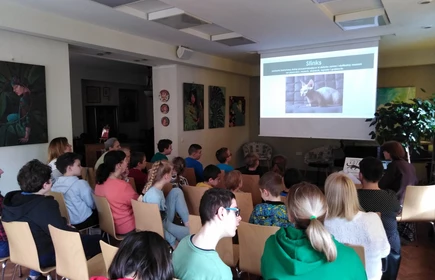 W dużej sali siedzi grupa osób zwrocona twarzami w stronę ekranu, na którym wyświetlana jest prezentacja.