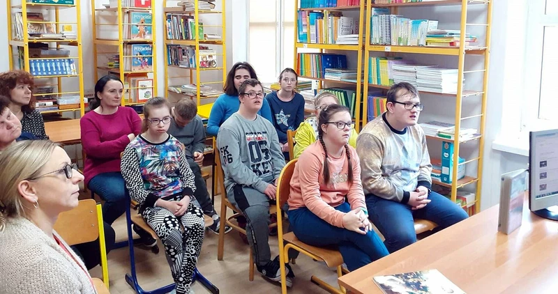 Grupa uczniów siedzi w bibliotece, w tle widać regały z książkami.